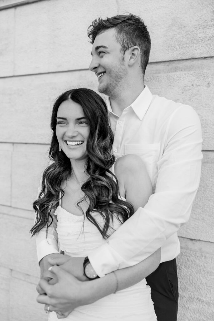 Romantic Des Moines engagement session featuring Molly and Tre’s surprise picnic at a local park with champagne, charcuterie, and matching t-shirts, followed by golden hour portraits in the gardens and architecture of Iowa State Capitol Park. Captured by Des Moines wedding photographer Koral Hull, the session blends candid laughter, romantic strolls, and playful moments that celebrate one step closer to “I Do.”